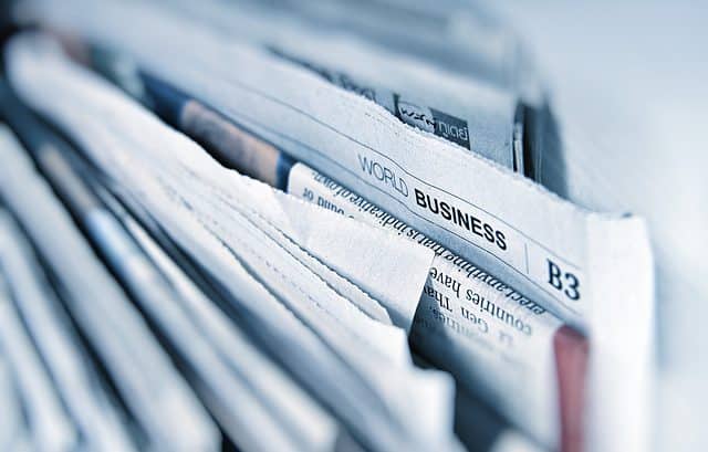 A close-up of several stacked newspapers with a visible headline section titled "World Business" on one of them, discussing topics like tax incentives and transfer pricing.