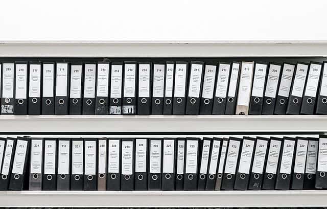 A neatly organized shelf holds numerous black ring binders, including the master file, all labeled and arranged in rows.