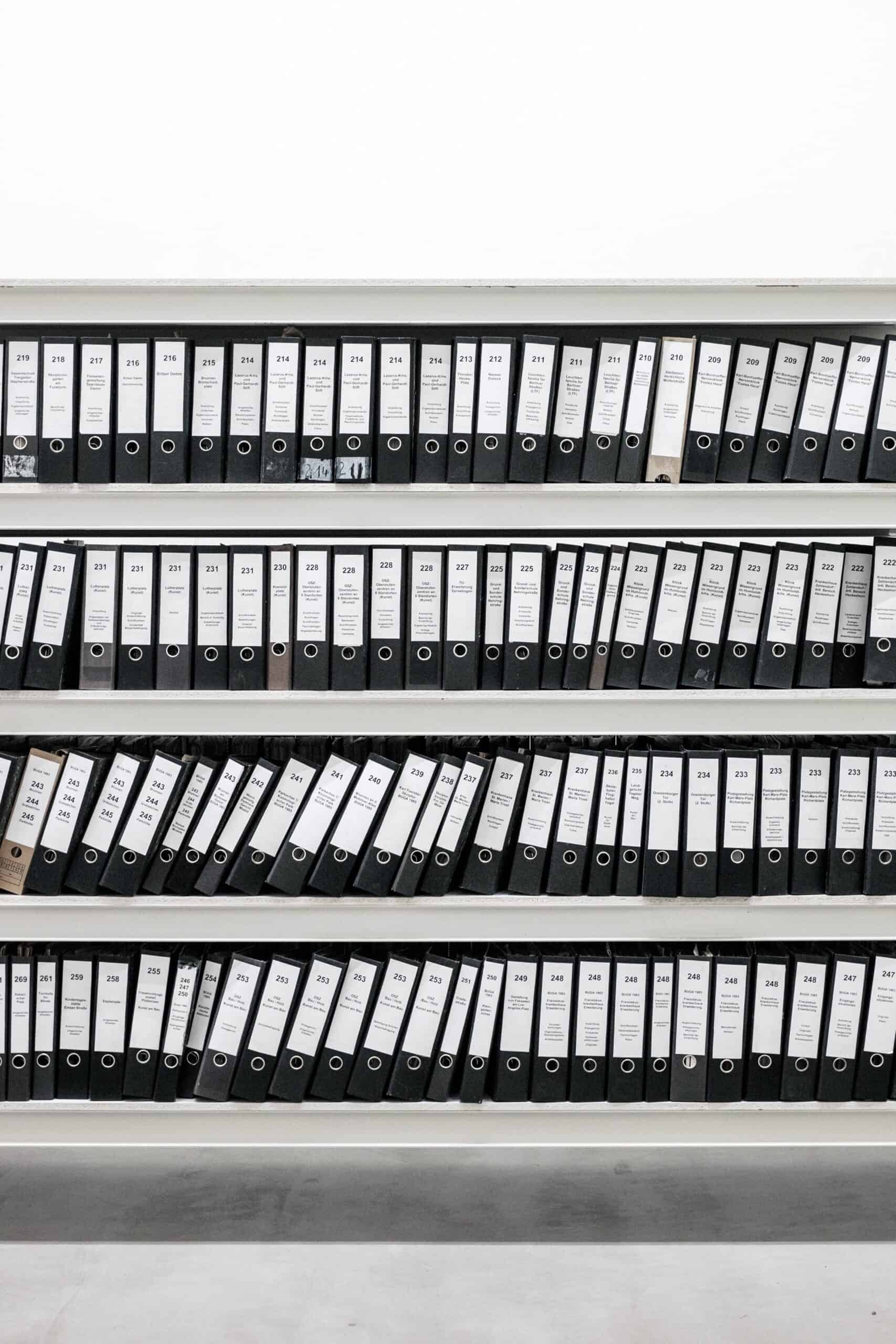 A neatly organized shelf holds numerous black ring binders, including the master file, all labeled and arranged in rows.