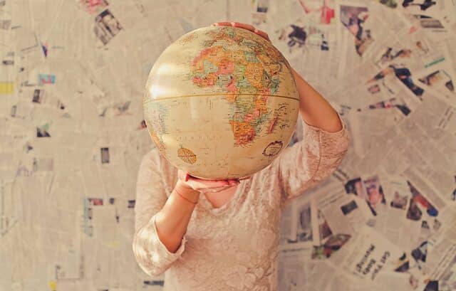 Person holding a globe in front of their face, standing against a wall covered in newspaper clippings, seemingly pondering transfer pricing considerations in Africa.