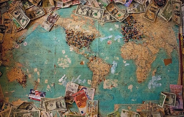 Worn world map covered with various currencies and pins marking locations across continents, much like a traveler’s journey navigating CbCR deadline extensions worldwide.