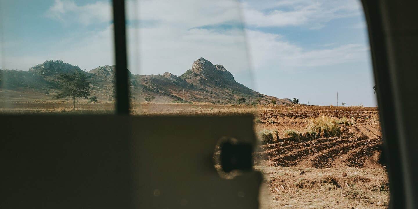 View of a rocky hill and an expansive field through the window of a vehicle on a clear day, as if the landscape itself were unbothered by Mozambique transfer pricing regulations.