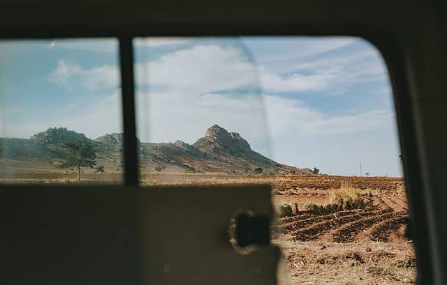 View of a rocky hill and an expansive field through the window of a vehicle on a clear day, as if the landscape itself were unbothered by Mozambique transfer pricing regulations.