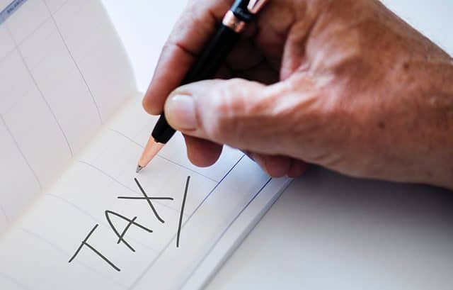 A hand holding a pen writing the word "TAX" in large letters on a piece of paper, highlighting recent Form ITR14 changes.