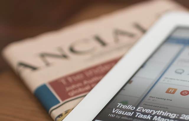 A tablet displaying a project management app screen is placed on top of a folded newspaper titled "Financial.