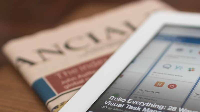 A tablet displaying a project management app screen is placed on top of a folded newspaper titled "Financial.