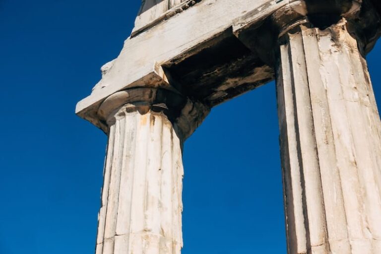 Two ancient stone columns, known as Pillar One and Pillar Two, with weathered surfaces stand under a clear blue sky.