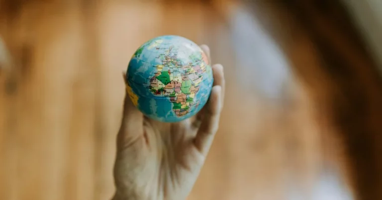 A hand holding a small globe showing parts of Europe, Africa, and Asia against a blurred brown background symbolizes the global impact of trends in transfer pricing.