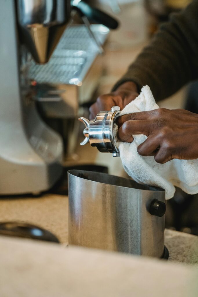 A person uses a cloth to clean a portafilter in front of an espresso machine on a kitchen counter, perhaps preparing for a discussion on transfer pricing.